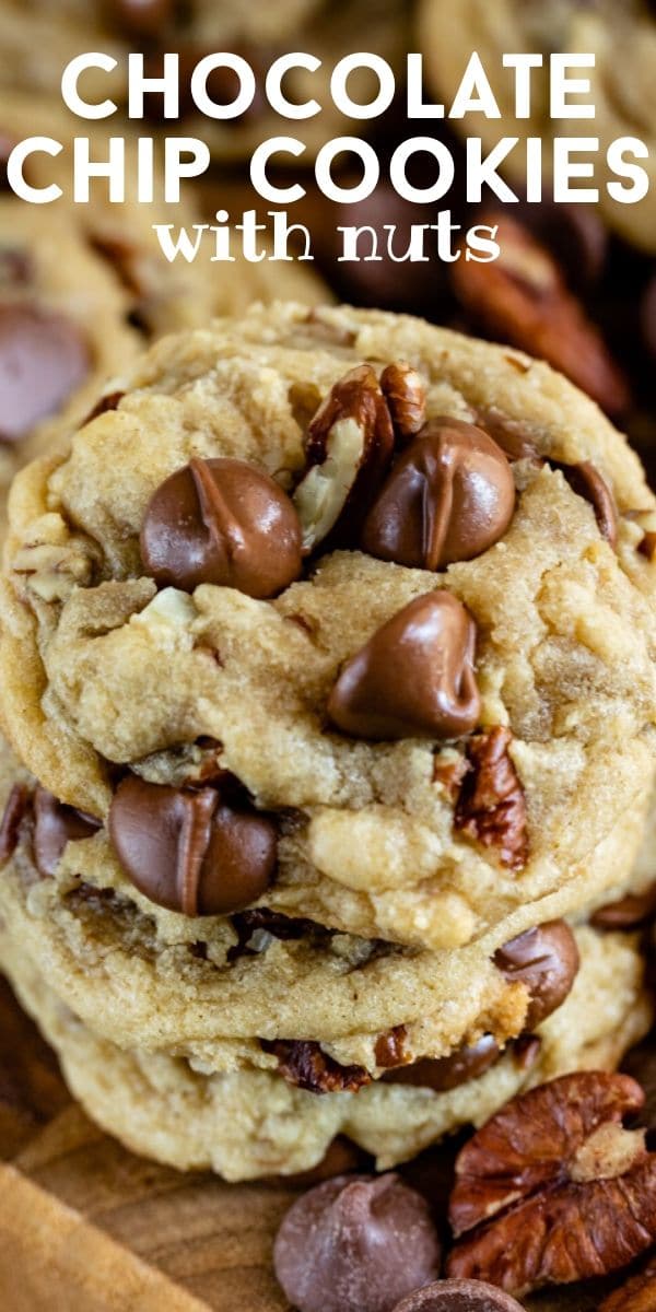 Overhead shot of chocolate chip pecan cookies stacked on a wood cutting board with chocolate chips and pecans and recipe title on top of image