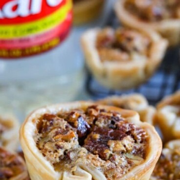 Mini pecan pies stacked on top of eachother with karo syrup in background
