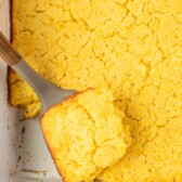 Overhead shot of jiffy corn casserole in a white baking dish with one corner piece being lifted out of dish