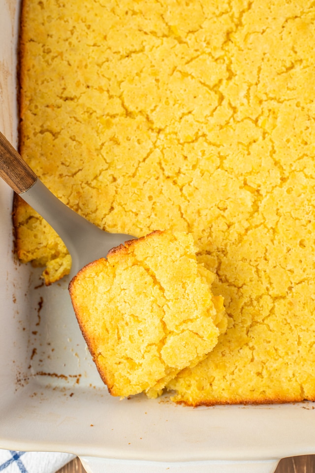 Overhead shot of jiffy corn casserole in a white baking dish with one corner piece being lifted out of dish