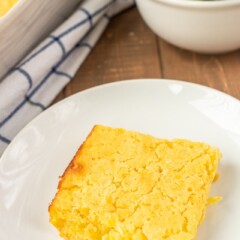 One slice of Jiffy Corn Casserole on a white plate with salad and rest of meal in background