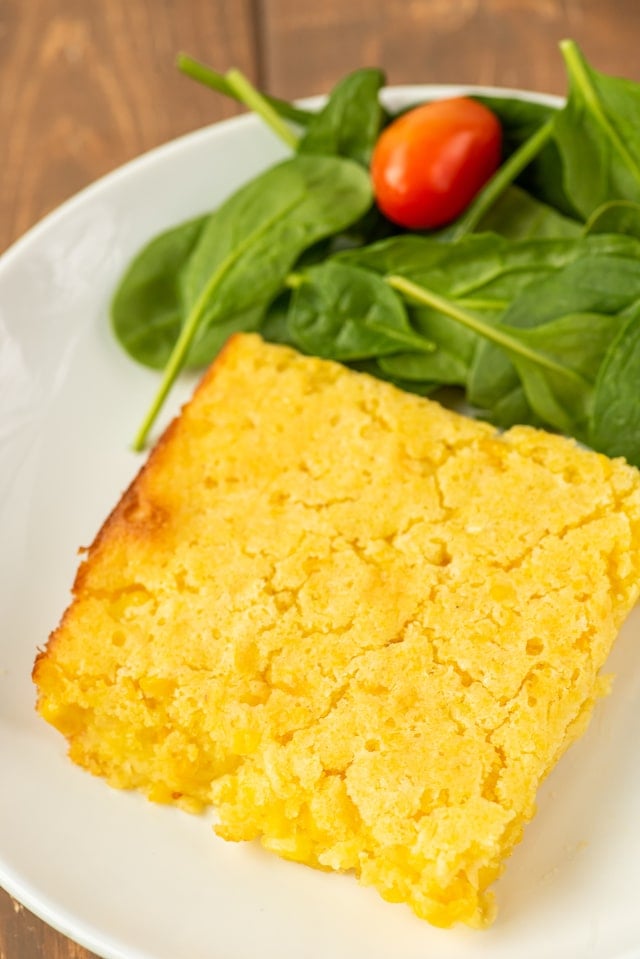 Close up of a piece of weight watchers corn casserole on a white plate with side salad next to it