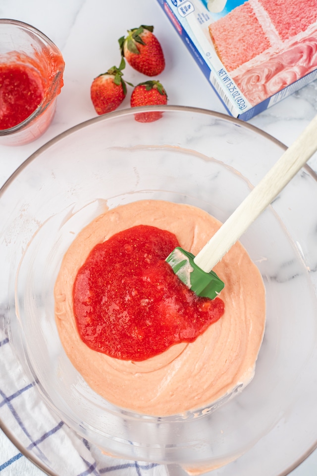 Overhead shot of strawberry purees being mixed into strawberry cake mix on top of kitchen counter