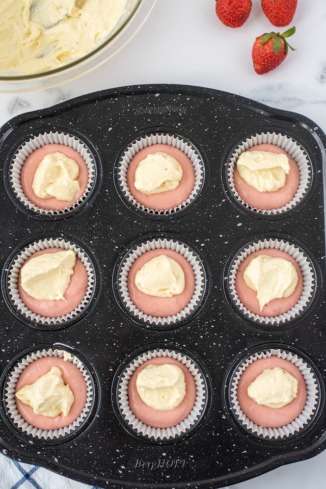 Overhead shot of raw cupcake batter in pan with cheesecake filling dollops on top
