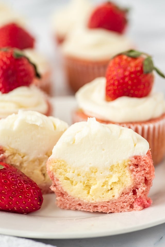 Strawberry cheesecake cupcakes on a white plate with front cupcake cut in half to show cheesecake filling