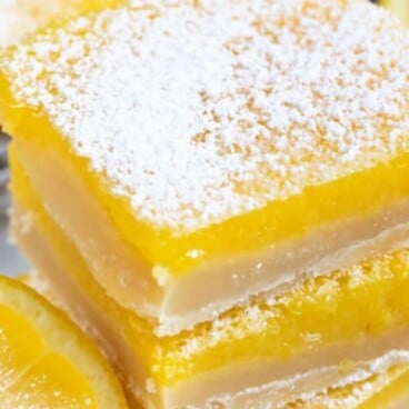 Overhead shot of stacked lemon bars with lemon wedges and powdered sugar on top and recipe title on top of image