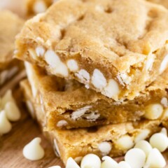 Stack of white chocolate blondies on a cutting board with white chocolate chips scattered around