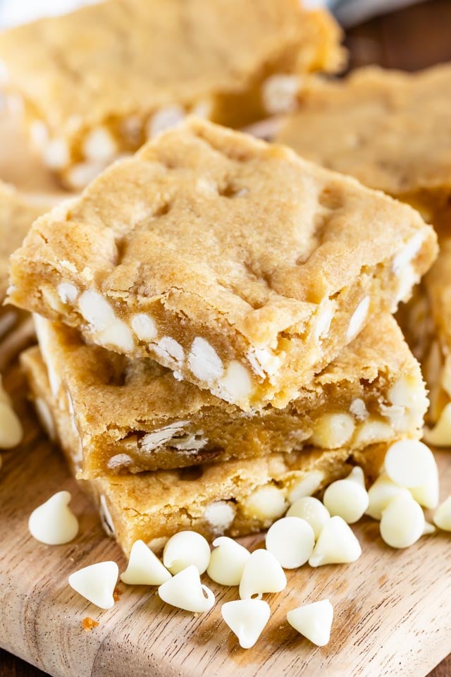 Stack of white chocolate blondies on a cutting board with white chocolate chips scattered around