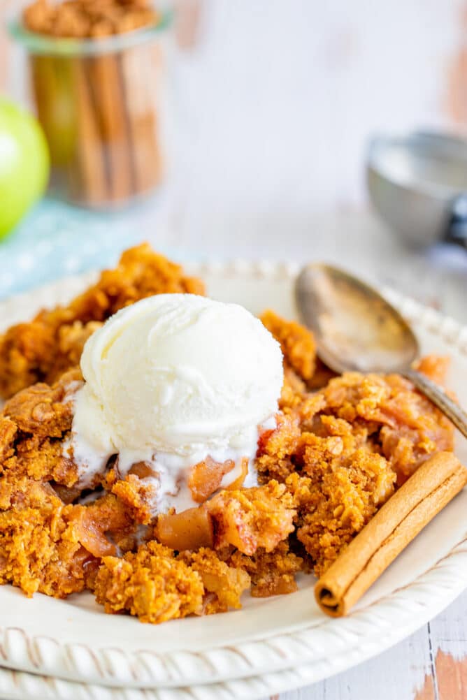 Apple dump cake on plate with vanilla ice cream, spoon and cinnamon sticks