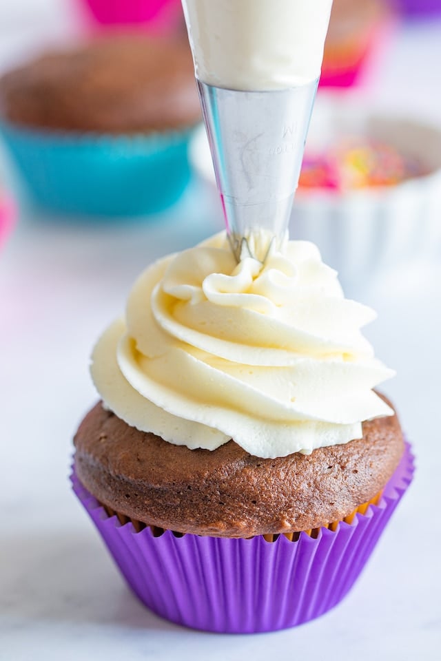 chocolate cupcake in purple liner being frosted