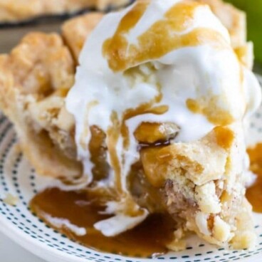 Slice of salted caramel apple pie on a blue dotted plate with vanilla ice cream and caramel on top and recipe title on bottom of image