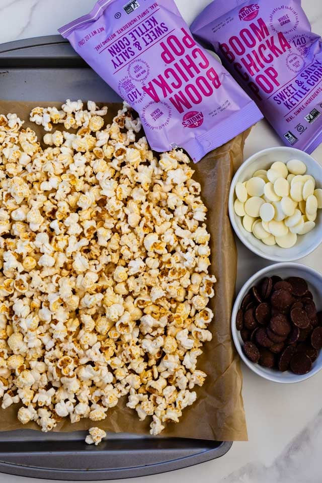 overhead photo of kettle corn on cookie sheet with bowls of chocolate and bags of Boom Chicka Pop