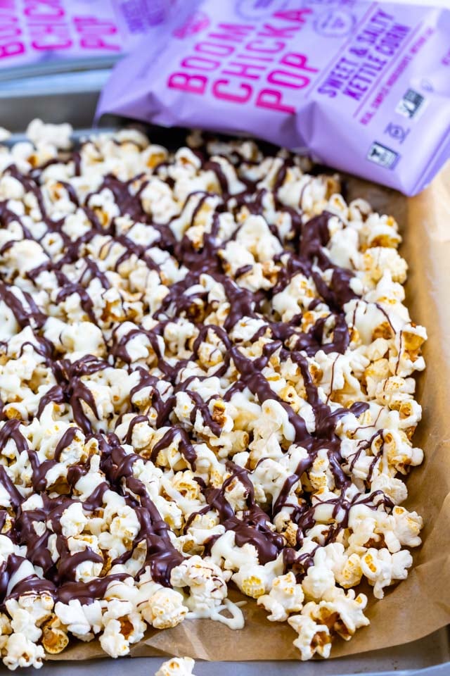 popcorn covered in chocolate on cookie sheet with popcorn bag behind