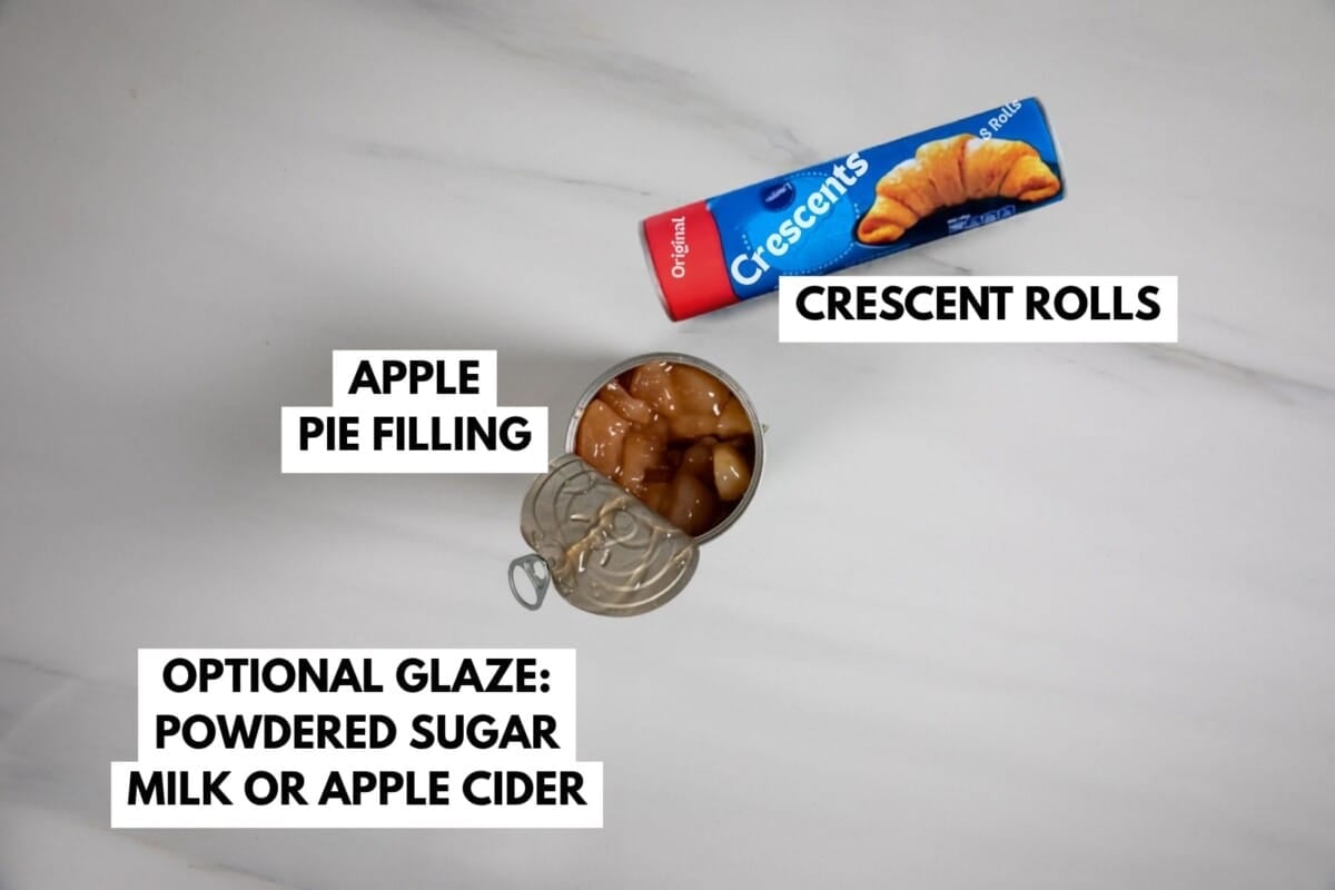 Ingredients for Apple Strudel on a white surface: a can of apple pie filling, a tube of crescent rolls, plus an optional glaze made with powdered sugar and milk or apple cider. Each item is clearly labeled with text.
