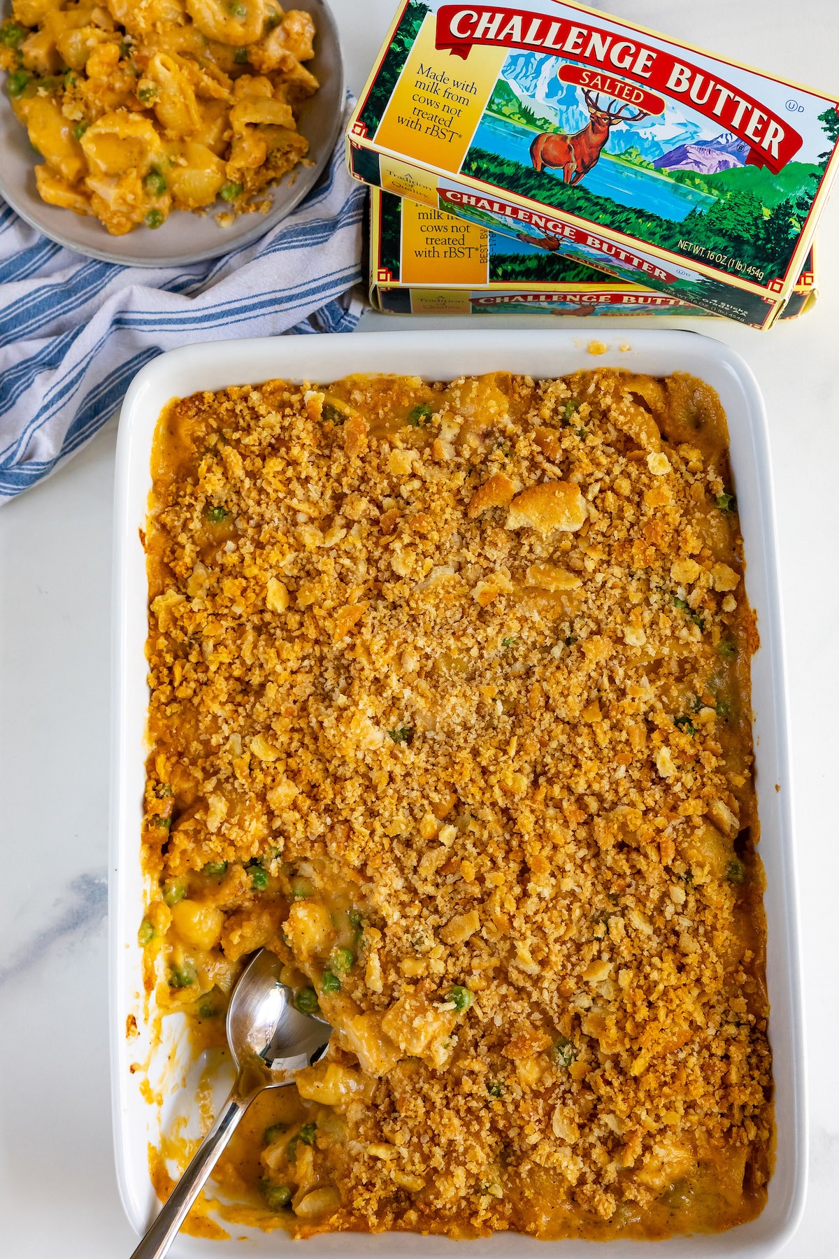 Overhead shot of easy cheesy chicken casserole in white baking dish with challenge butter next to it