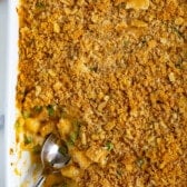A baking dish brims with cheesy chicken casserole, its golden breadcrumb crust glistening invitingly. A serving spoon rests inside, uncovering tender chicken pieces and vibrant vegetables beneath, creating a delightful masterpiece for the senses.