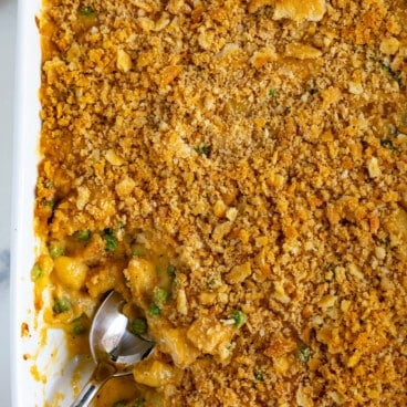 A baking dish brims with cheesy chicken casserole, its golden breadcrumb crust glistening invitingly. A serving spoon rests inside, uncovering tender chicken pieces and vibrant vegetables beneath, creating a delightful masterpiece for the senses.