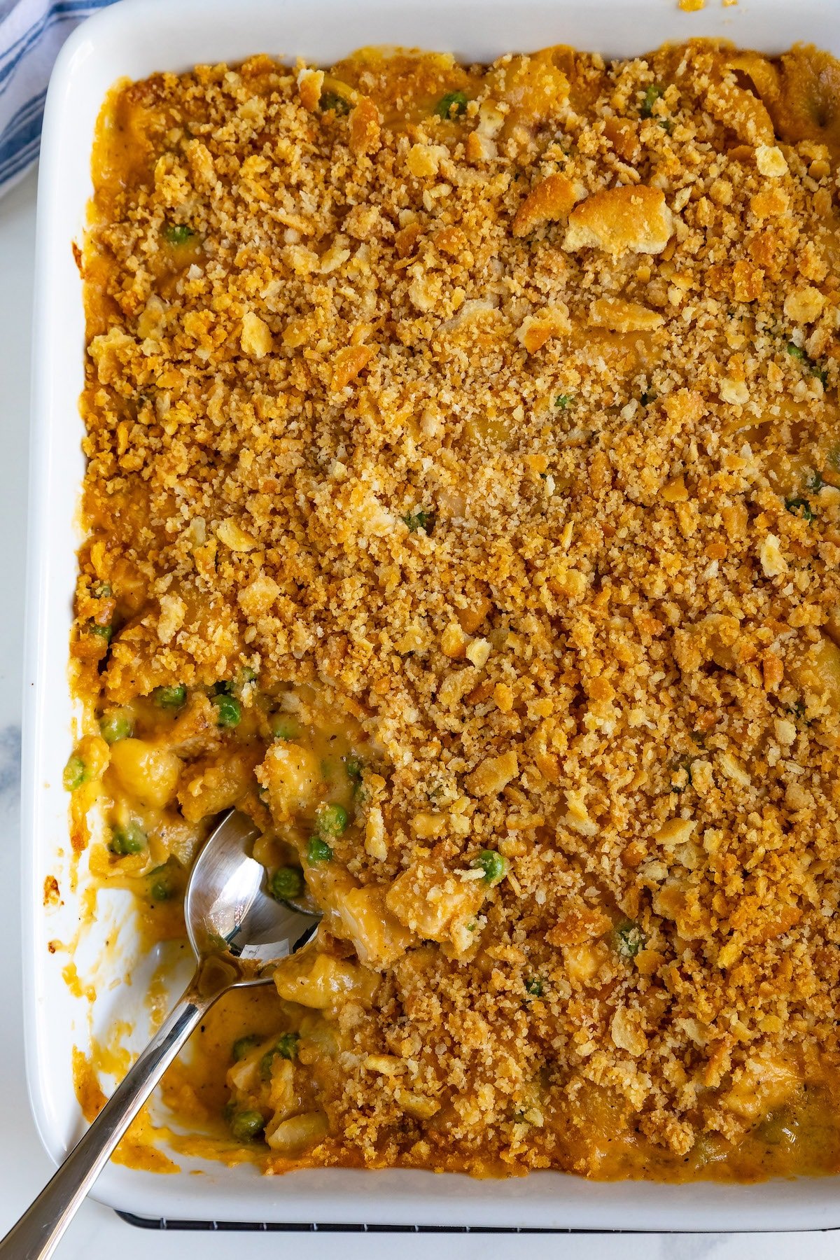 A baking dish brims with cheesy chicken casserole, its golden breadcrumb crust glistening invitingly. A serving spoon rests inside, uncovering tender chicken pieces and vibrant vegetables beneath, creating a delightful masterpiece for the senses.