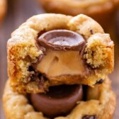 Close up of chocolate chip cookie cups stacked on top of eachother with top cut in half to show rolo filling with recipe title on top