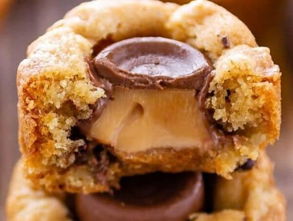 Close up of chocolate chip cookie cups stacked on top of eachother with top cut in half to show rolo filling with recipe title on top