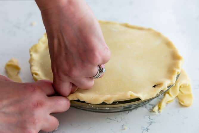 Crimping the edges of the top pie crust in a pie dish before baking