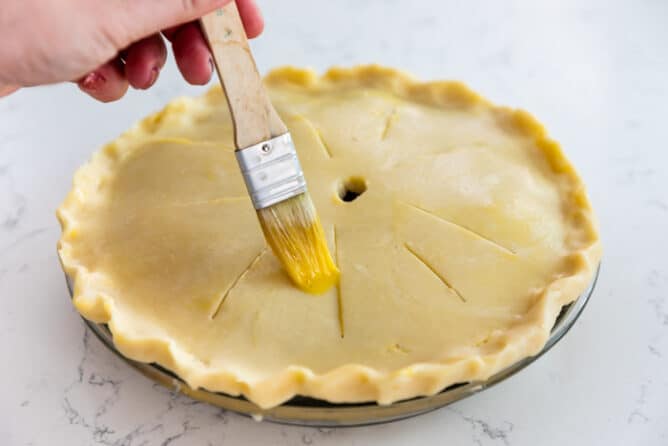 Brushing the top pie crust with egg wash before it bakes