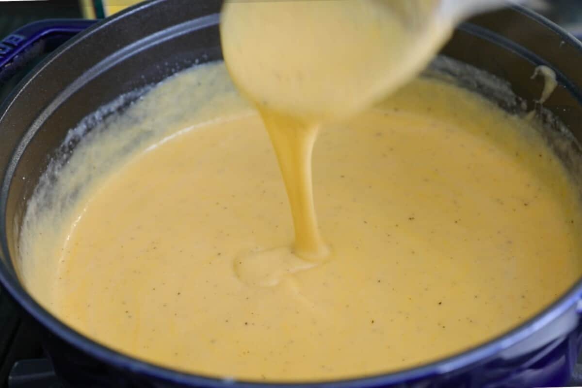 A creamy yellow sauce being stirred in a blue pot, perfect for a cheesy chicken casserole. Its texture appears smooth and thick, with small flecks of seasoning visible throughout.
