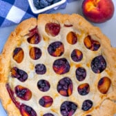 Overhead shot of peach blueberry pie on kitchen counter with fresh peaches and blueberries next to it