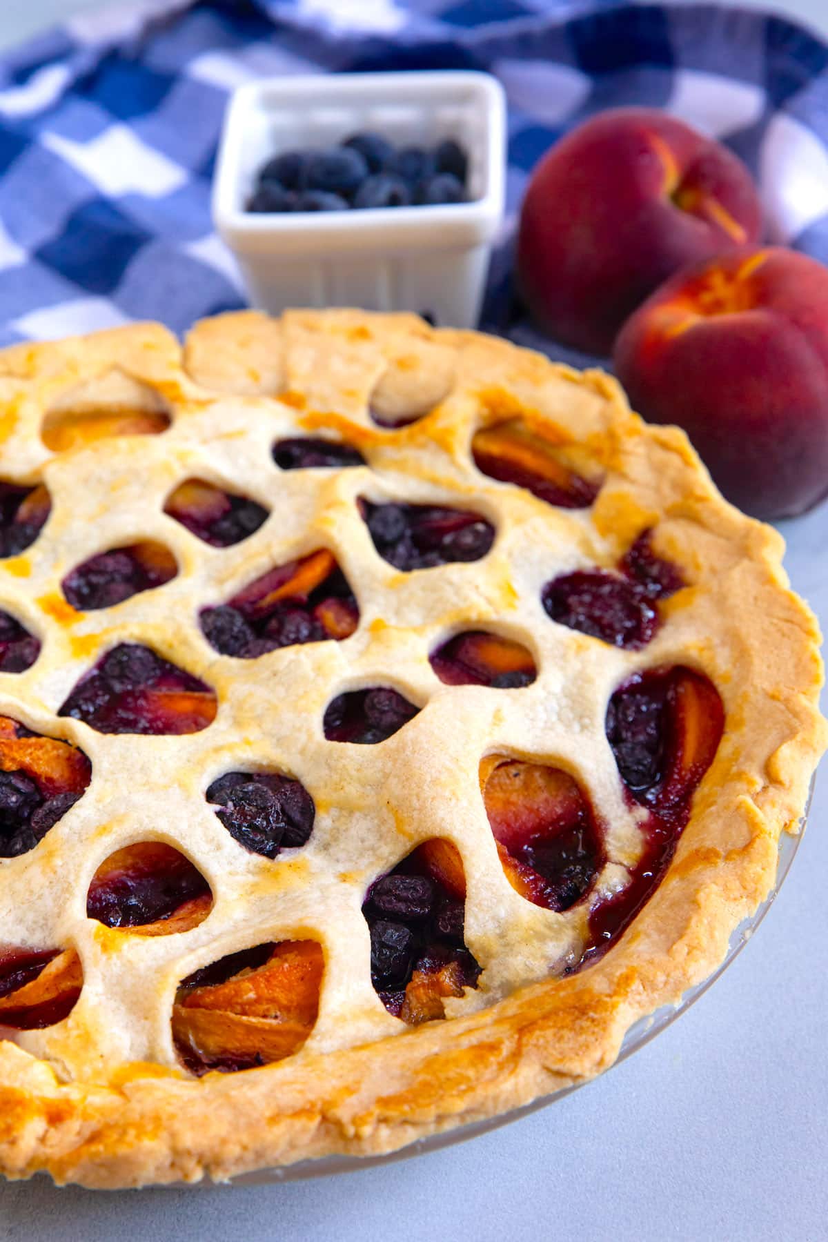 Close up shot of peach blueberry pie in a pie dish with fresh fruit behind it