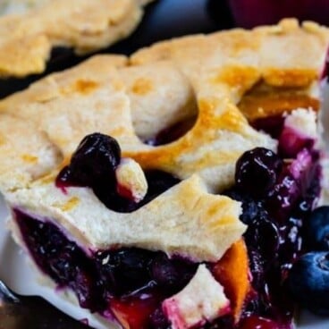 Close up shot of peach blueberry pie slice on a white plate with recipe title on top