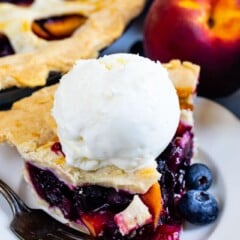 Slice of peach blueberry pie on a white plate with a scoop of vanilla ice cream on top