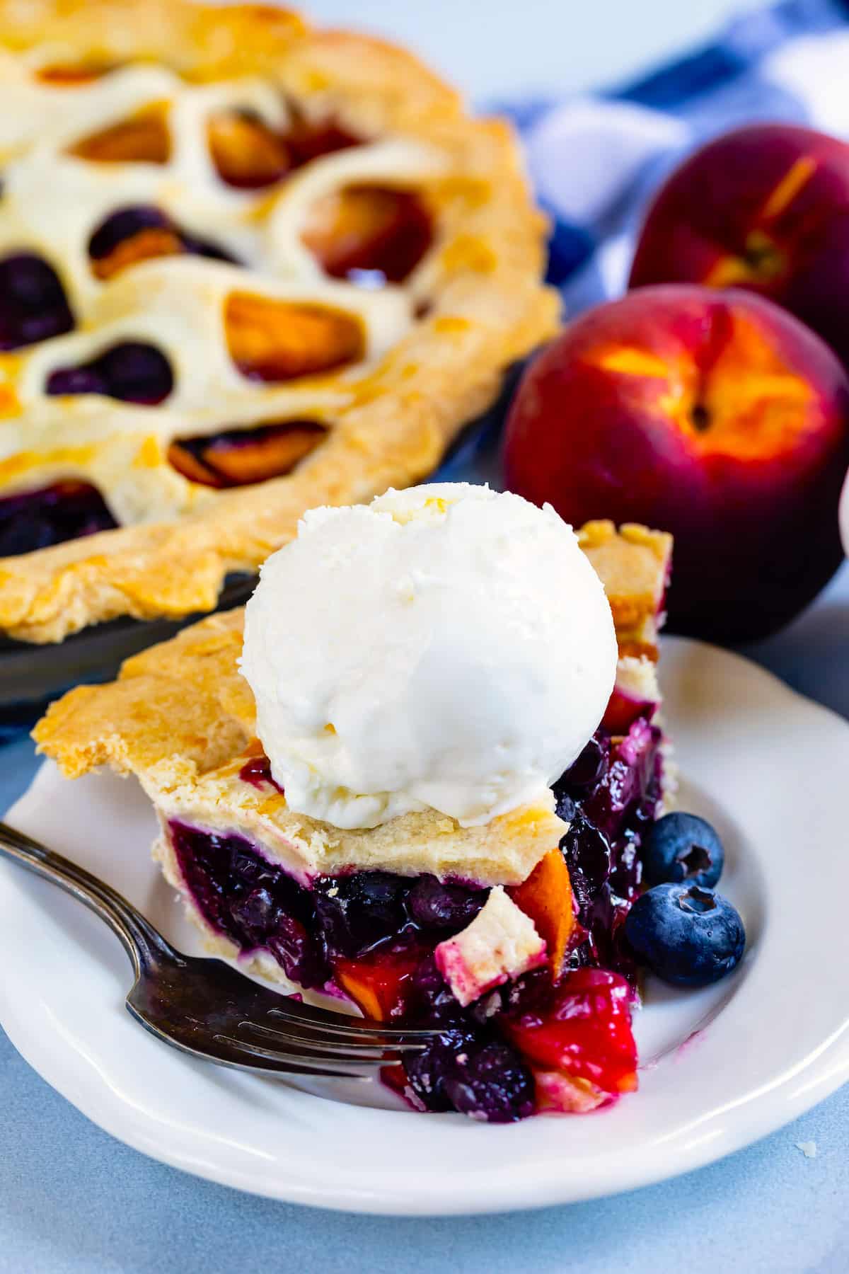 Slice of peach blueberry pie on a white plate with a scoop of vanilla ice cream on top