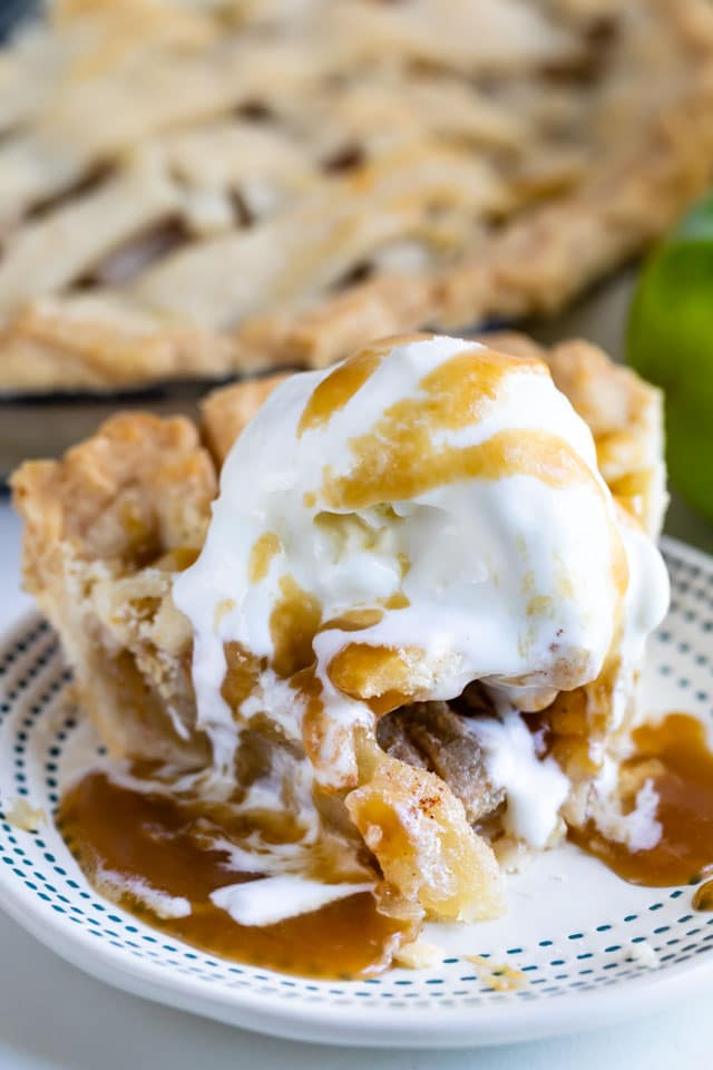 Slice of salted caramel apple pie on a blue dotted plate with vanilla ice cream and caramel on top