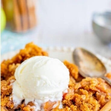 Apple dump cake on plate with vanilla ice cream, spoon and cinnamon sticks with recipe title on top of image