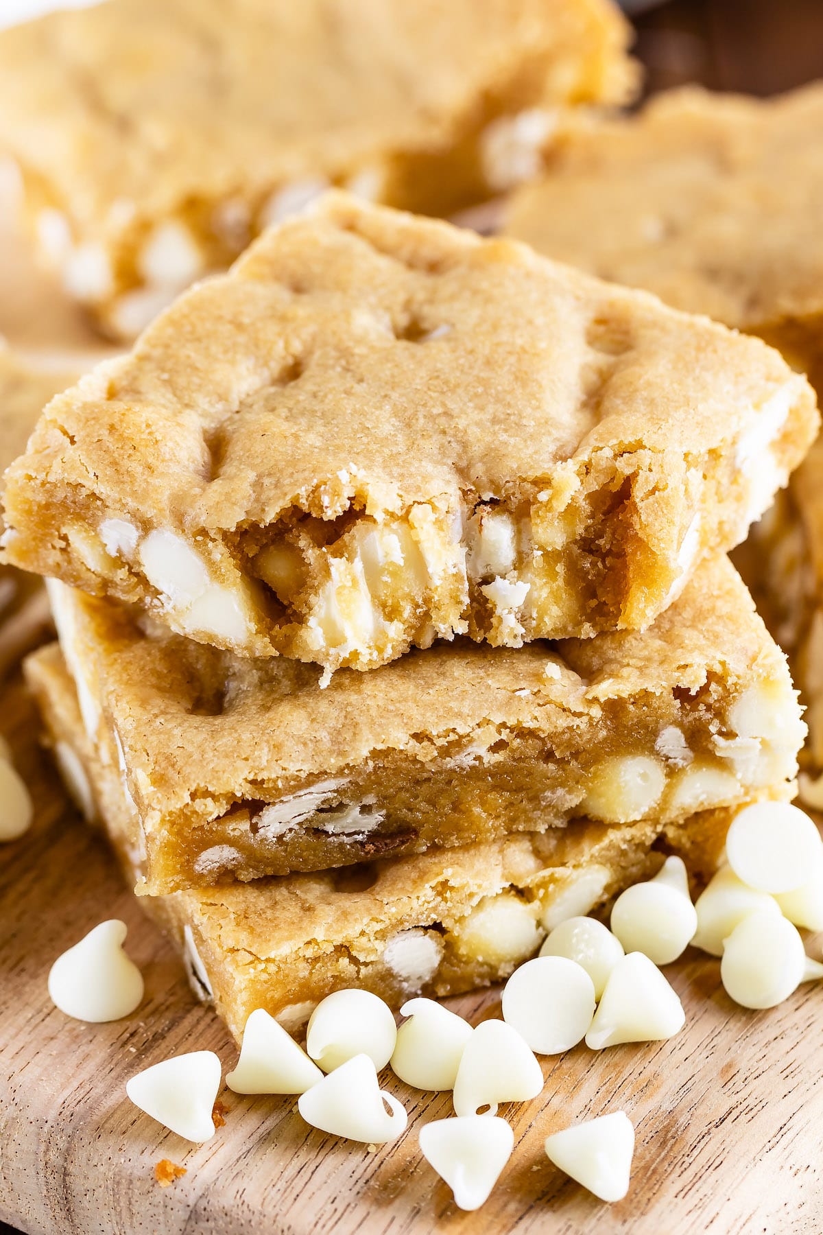 stack of 3 blondies with white chocolate chips top one with bite missing.