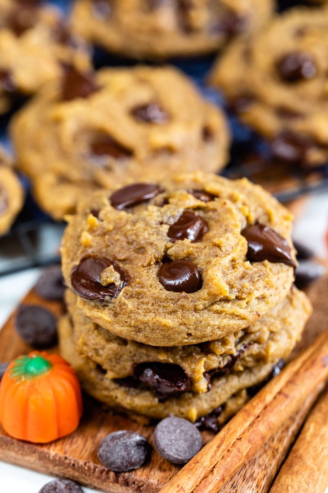 Stack of pumpkin chocolate chip cookies with ingredients around them and more cookies in background