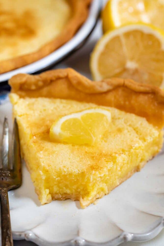 Slice of lemon chess pie with one bite missing on a white scalloped plate