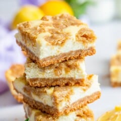 Stack of lemon cheesecake bars on counter with lemon slices and mint leaves on counter