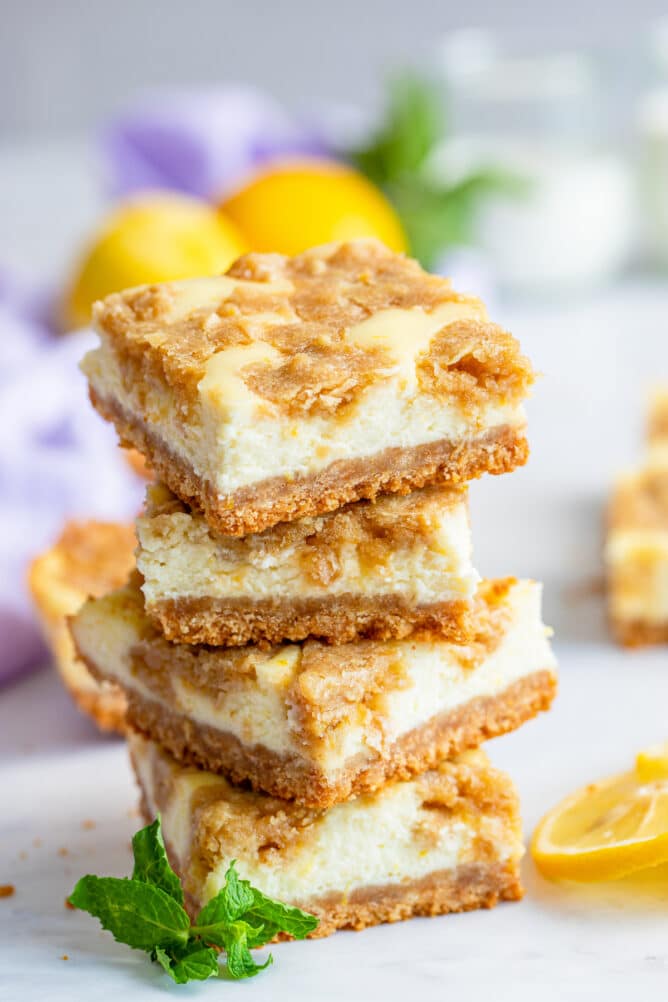 Stack of lemon cheesecake bars on counter with lemon slices and mint leaves on counter