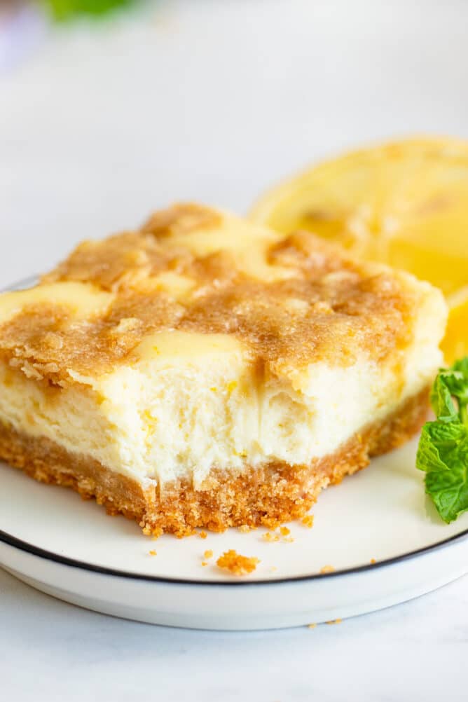 Lemon cheesecake bar on a plate with one bite missing from corner