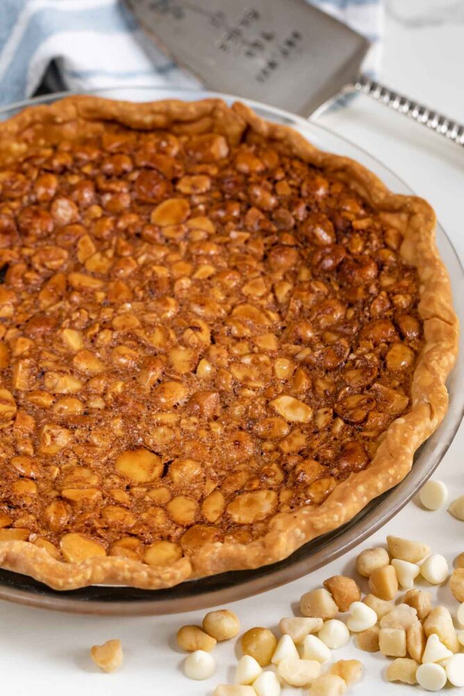 Overhead view of white chocolate macadamia nut pie with white chocolate chips and macadamia nuts on counter next to pie