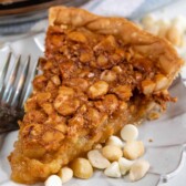 One slice of macadamia nut pie on a white scalloped plate with extra white chocolate chips and macadamia nuts