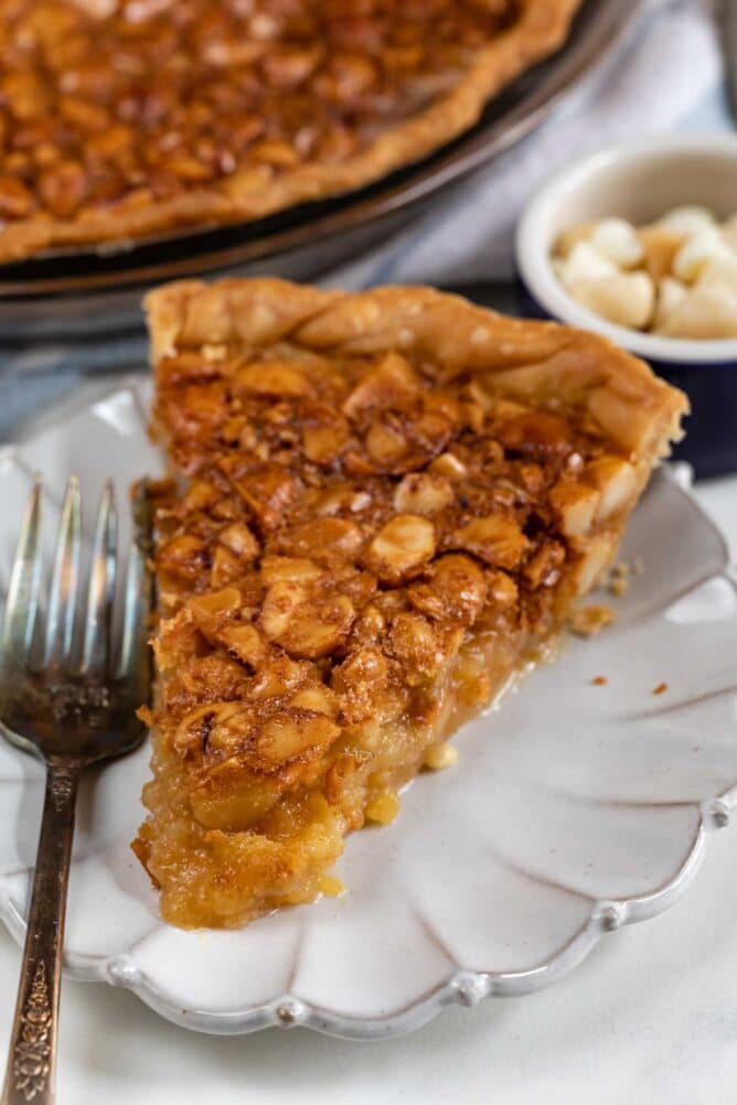 Slice of macadamia nut pie on a white scalloped plate with silver fork