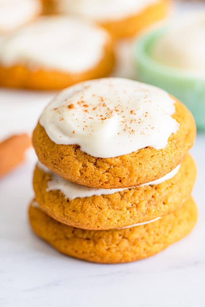 Stack of three pumpkin cookies topped with cream cheese frosting and pumpkin spices
