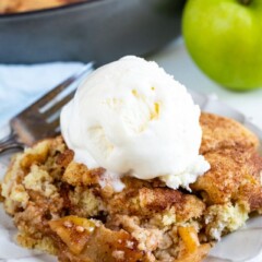 Snickerdoodle apple cobbler on a white plate with vanilla ice cream scoop on top and green apple in background