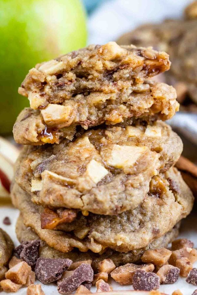 Large stack of apple cookies with top cooke split in half to show apple and toffee bits inside the cookie