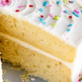 Layered yellow cake with vanilla frosting and rainbow sprinkles with slice cut out and recipe title on image