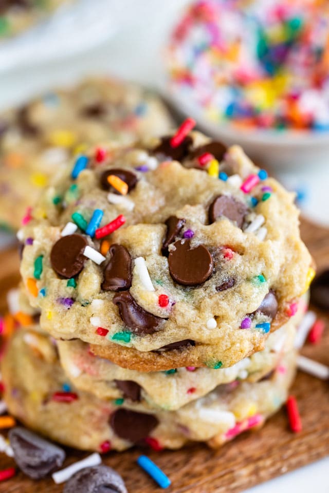 Close up shot of three birthday cookies with rainbow sprinkles stacked on eachother on top of a wood cutting board