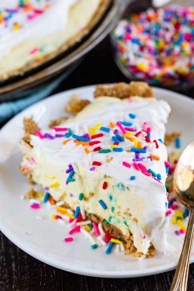 Slice of funfetti pie on a white plate with silver spoon and sprinkles in the background