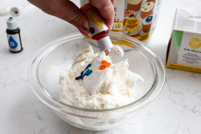 hand squeezing yellow food coloring into bowl of white frosting